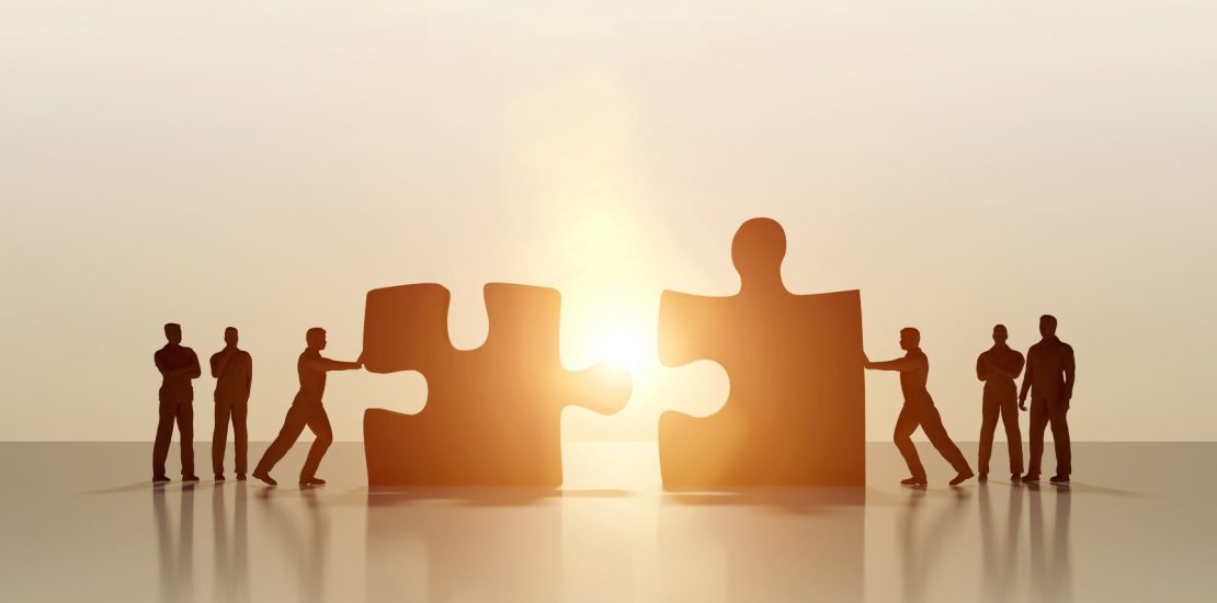 Group of business men supporting two of them pushing jigsaw puzzle pieces together, creating connection as a result of successful teamwork, partnership and finding solutions. Brightly lit image with dark silohuettes on a background illuminated by sunlight with lens flares. Clean and modern, empty set with copy space. Digital generated image and characters.